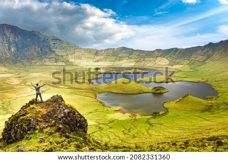 The landscape of Corvo Island in the Azores with man on rock peak with open arms. Concept of freedom and travel adventure. Royalty-Free Stock Photo #2082331360