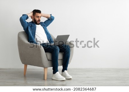 Terrified Arab freelancer looking at laptop screen, grabbing his head, making mistake in business project, missing deadline against white studio wall, copy space. Young man having online work stress Royalty-Free Stock Photo #2082364687