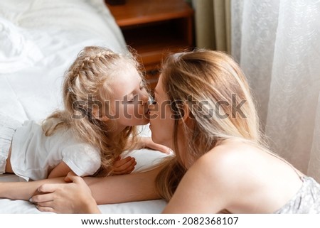 Beautiful gentle child girl kissing mom on nose at home in bedroom. Loving and caring mother show tenderness love to her daughter kid. Kiss on mother's day in A happy family