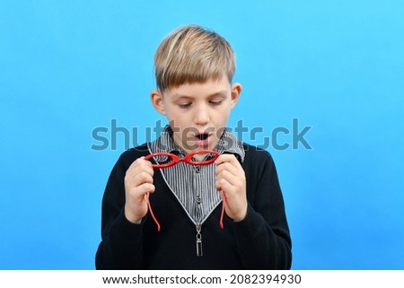 The boy breathes on red glasses in which there are no glasses to wipe the lenses.