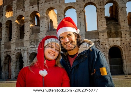 A lovely young couple taking a picture in front of the Colosseum with red Santa hats. Feeling of happiness and love. Christmas vacation concept.