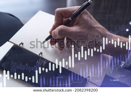 A trader in formal wear writing down some quotes to research stock market trends using smart phone for right investment solutions. Wealth management concept. Hologram Forex chart over close up shot.