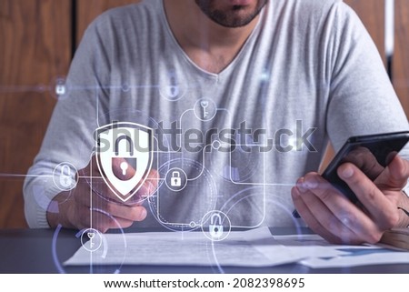 A businessman in casual wear signing the contract to prevent probability of risks in cyber security. Checking the phone. Padlock Hologram icons over the working desk.