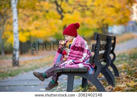 Happy child, playing with in autumn park on a sunny day, foliage and leaves all around him, eating apple