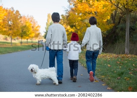 Happy children, playing with pet dog in autumn park on a sunny day, foliage and leaves all around them