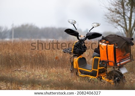 The motorcycle has an orange back bag to deliver food to home, stand on the dryed field.
