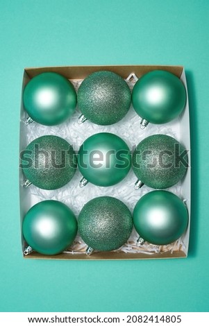 Top view of cardboard box with collection of green christmas balls. Concept of Xmas and New Year. Beautiful decorations for winter events, holidays and greetings. Isolated on green background