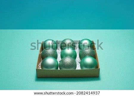 Cardboard box with collection of green christmas balls. Concept of Christmas and New Year. Beautiful decorations for winter events and holidays. Isolated on green and turquoise background. Copy space