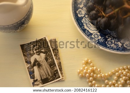 This suggests reminiscing over old photographs and memories.  Pearls, grapes, old photographs, and a small jug sit atop a weathered table.  Filtering effect is done in camera.
