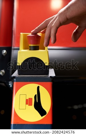 A man's hand touches a red emergency stop signal button, in production.