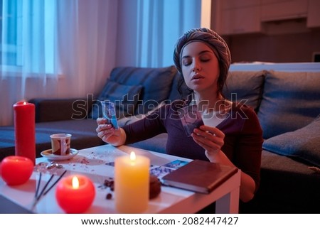 Serious concentrated fortune-teller staring at oracle cards in her hands Royalty-Free Stock Photo #2082447427