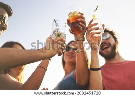 Friends clinking alcoholic cocktail glasses together - Carefree young people in summer drinking and toasting of friendship. Shallow DOF with focus on the left one glass Royalty-Free Stock Photo #2082451720