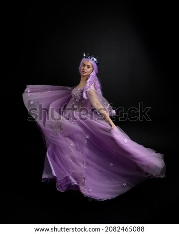 Full length portrait of girl wearing purple flower fairy ball gown and  fantasy princess crown. Standing pose with gestural hand movements as if casting magical spells.  isolated on dark studio backgr