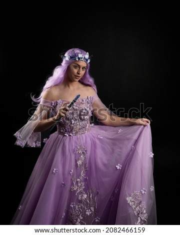 portrait of girl wearing purple flower fairy ball gown and  fantasy princess crown. Standing pose with gestural hand movements as if casting magical spells.  isolated on dark studio background 