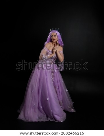portrait of girl wearing purple flower fairy ball gown and  fantasy princess crown. Standing pose with gestural hand movements as if casting magical spells.  isolated on dark studio background 