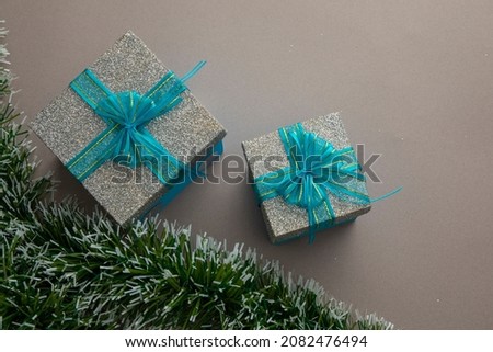 Two silver gifts and blue bow with green garland and brown background for text.