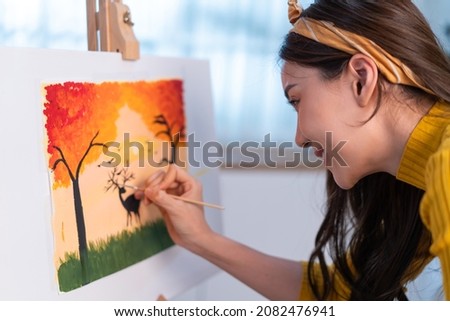 Asian young talented woman artist coloring on painting board in house. Attractive beautiful female draw art picture, creating artwork with watercolor paint and brush enjoy creativity activity at home.