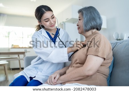 Asian nurse at nursing home take care of disabled senior elderly woman. Beautiful therapist doctor measure heart rate by stethoscope on female older patient on sofa. Medical insurance service concept.