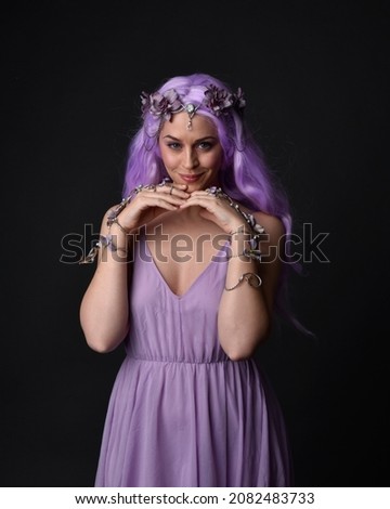 portrait of girl wearing purple fantasy dress with fairy wings and crown. pose with gestural hand movements as if casting magical spells.  isolated on dark studio background 