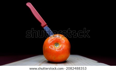 Concept of high price rise of tomato where tomato stabbed with knife using of chopstick and dark background. Royalty-Free Stock Photo #2082488353