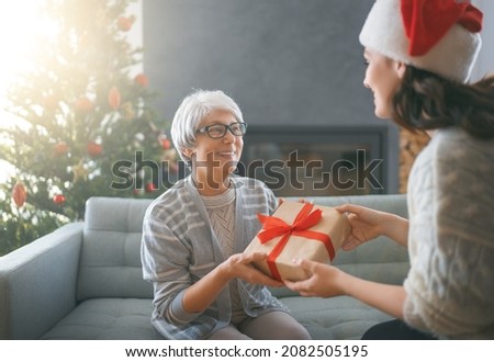 Merry Christmas, Happy Holidays. Senior mom and her adult daughter exchanging gifts. Having fun near tree indoors. Loving family with presents in room. 