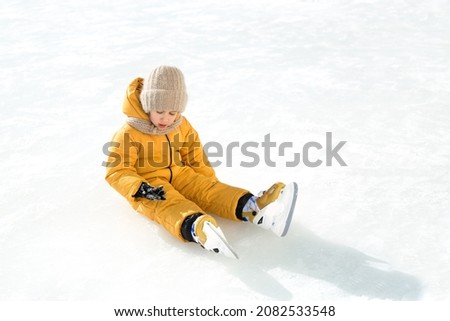 The girl fell on the ice, taking her first steps on skates. A child learns to skate. A child sits on an ice rink and examines mittens that were injured during the fall. Ice skating season on the pond 