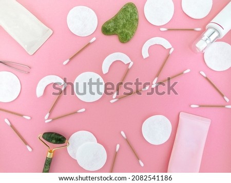 the number 2022 is lined with disks and cotton swabs, around are cosmetics, creams and cleansing foam, a guache massager on a pink background
