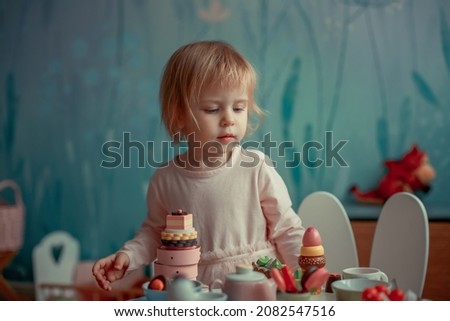 Cute little girl is playing in doll tea party at home. Image with selective focus, noise effect and toning