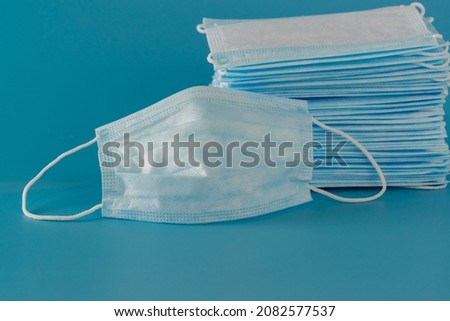 There are many new medical surgical three-layer masks stacked high and one mask lies next to the blue background