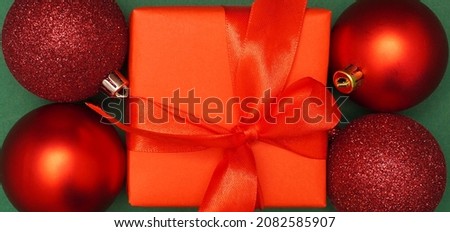 Creative concept of Christmas or New Year red colored decoration Christmas gift and baubles over green background. Greeting card. Minimal concept.                               