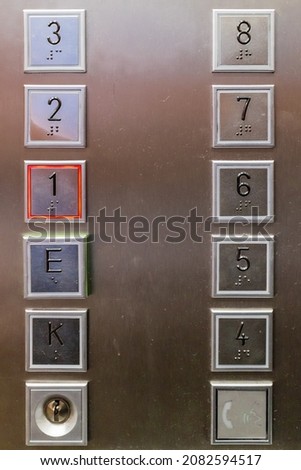 Straight on close up view of twelve heavy duty square elevator buttons in stainless steel surface