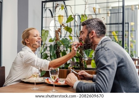 A blond, elegant woman sitting in the restaurant with her man and feeding him. A happy couple at romantic dinner at a restaurant. A couple in the restaurant
