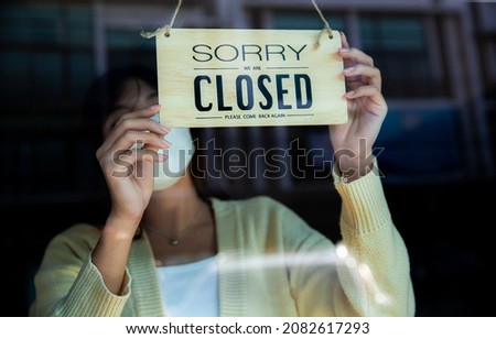 Asian woman wearing face mask turn on sorry we are closed signage on the front door for covid-19 lockdown.