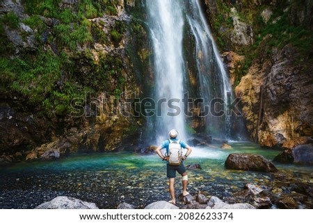 A man in a hat stays under the streams of the waterfall. Grunas Waterfall is a picturesque site inside the National Park of Thethi, Albania