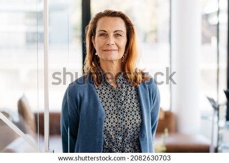 Stylish confident businesswoman with air of authority standing in front of a high key office looking at the camera with a friendly smile Royalty-Free Stock Photo #2082630703