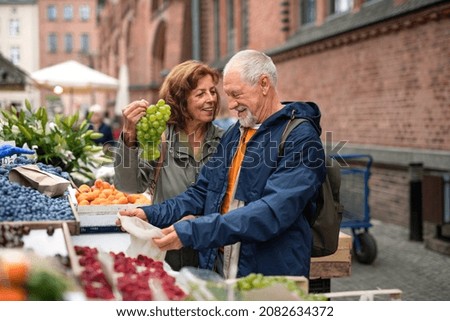 Happy senior couple tourists buying fruit outdoors on market in town. Royalty-Free Stock Photo #2082634372