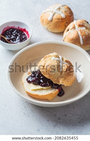 Traditional Easter cross buns with raisins, butter and berry jam on gray background.