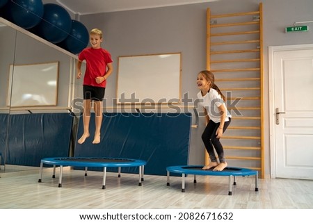 Little girl and a boy jumping on a trampoline in the gym and having fun. Image contains little noise   Royalty-Free Stock Photo #2082671632
