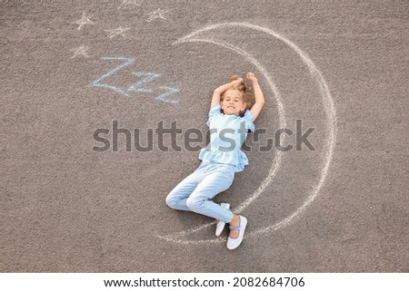 Little girl lying near chalk drawing of moon outdoors