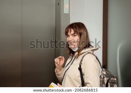 A young woman with a backpack stands by the elevator and smiles.