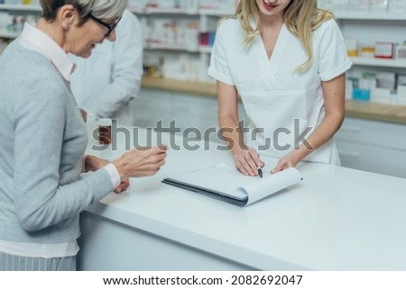 Young female pharmacist giving prescription to sign to a smiling senior female customer in a pharmacy
