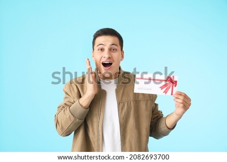 Surprised young man with gift card on color background