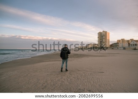 Man with black jacket on a beach in winter with his photo camera