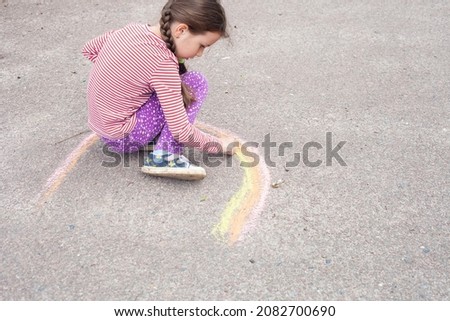 a girl of European appearance with pigtails draws a rainbow on the asphalt