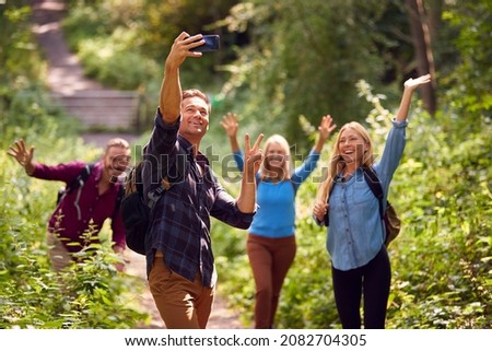 Group Of Friends Posing For Selfie In Countryside Taking Picture On Phone As They Hike Along Path