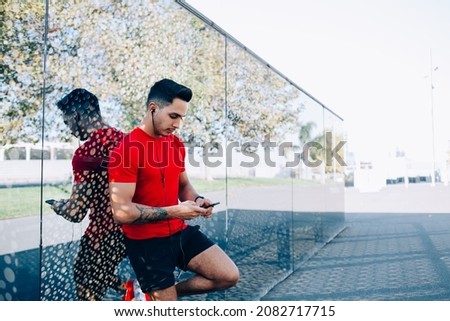 Caucasian man in sportswear creating publication about cardio exercises for sharing info to sport blog using wireless 4g internet on mobile phone, male runner in headphones choosing media for listen