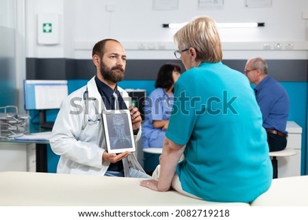 Doctor holding tablet with radiography for osteopathy diagnosis in medical office. Senior patient looking at x ray scan on gadget display for orthopedic analysis and rehabilitation.