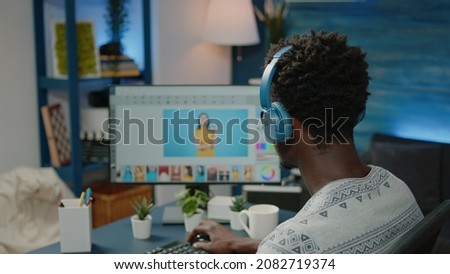 Photographer retouching pictures on computer and wearing headphones. Man working as media illustrator doing editing work on monitor for photography production. Image editor using app