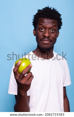 Portrait of man holding green apple in hand and looking at camera. Vegetarian person with healthy fruit for organic diet and nutrition in studio. Adult with raw freshness for vitality