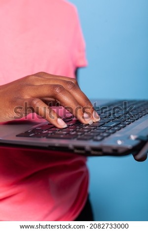 Closeup of african american teenager hands browsing online information working at business project typing marketing strategy on laptop computer. Young woman standing in studio with blue background